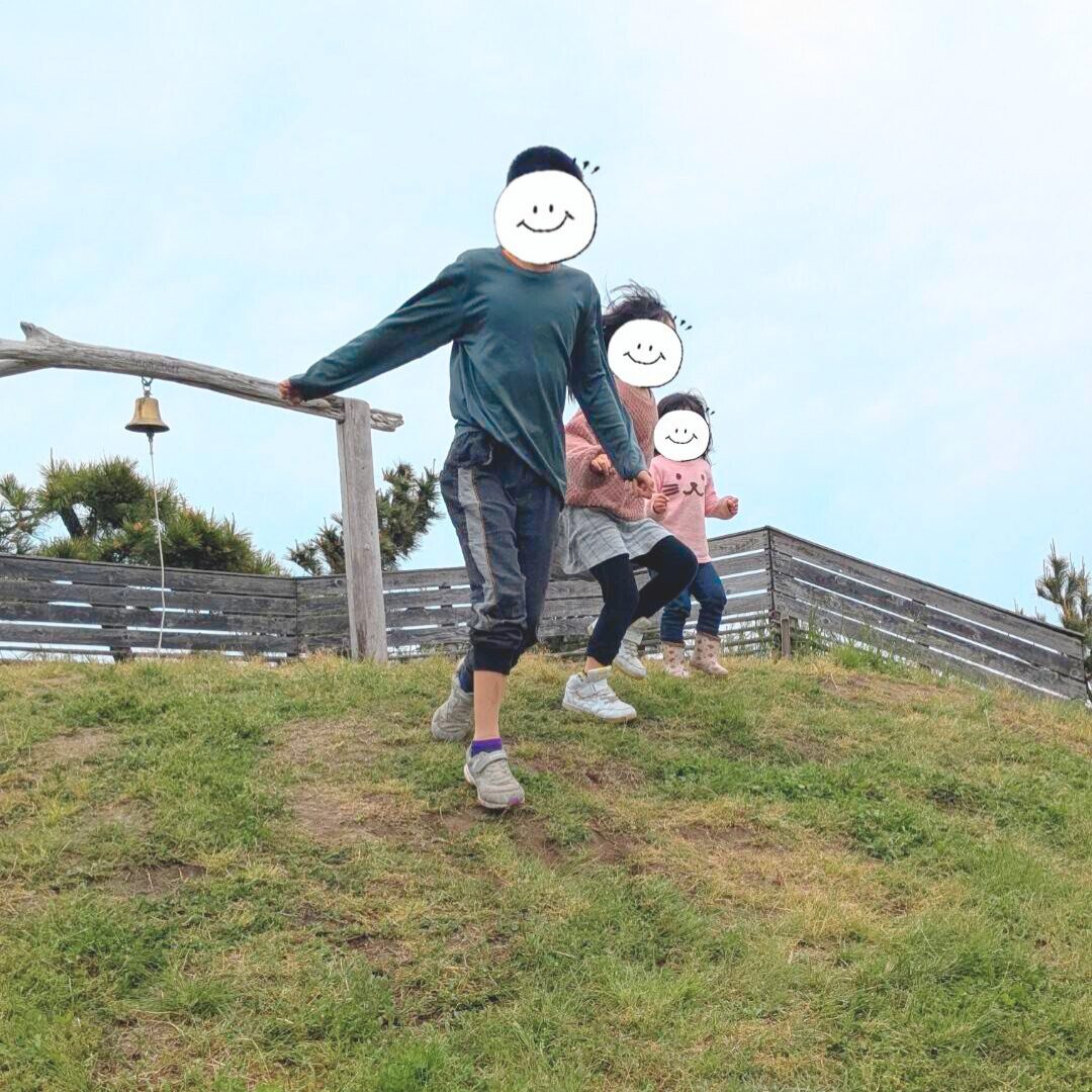 緑の丘の上からかけ降りる３人の子どもたちの様子