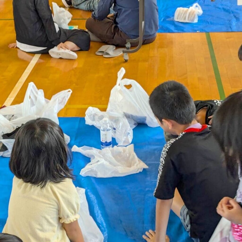 地域の避難所になっている小学校に行って、ブルーシートに座っている、二人の子どもの後ろ姿の写真