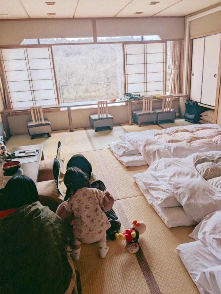 布団が敷いてある旅館の部屋でくつろぐ３人の女の子の後ろ姿の写真。