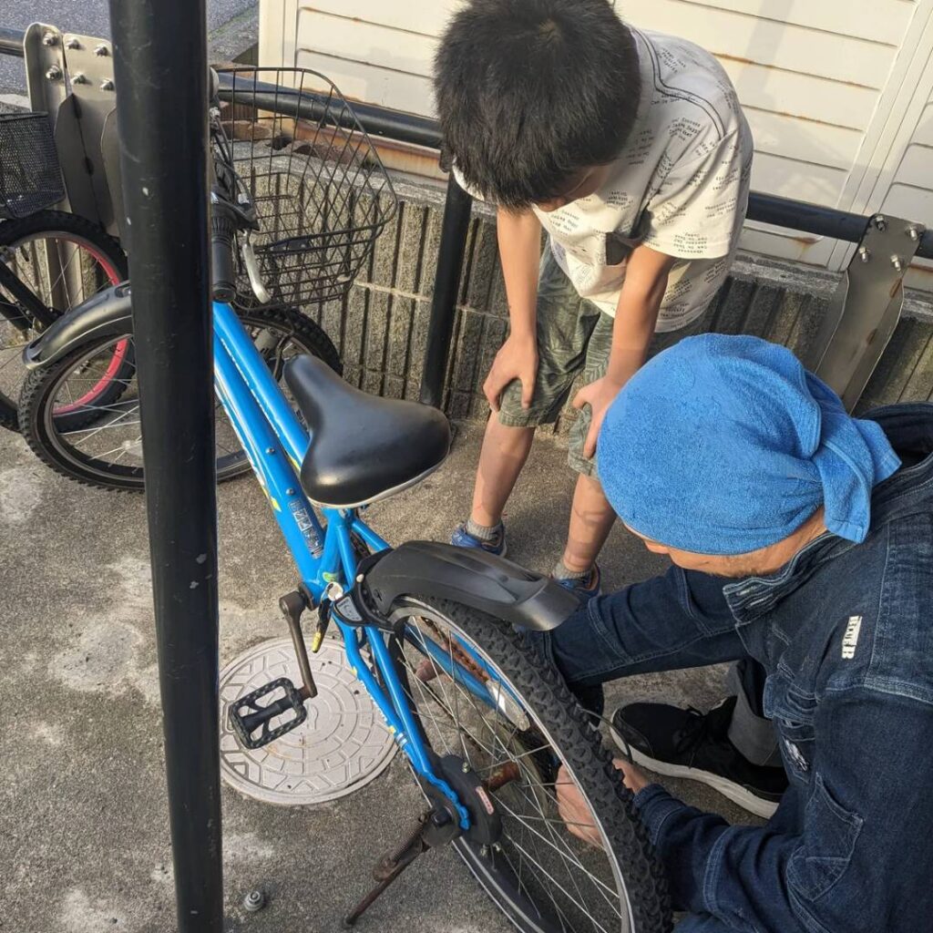 自転車の外れたチェーンを直すお父さんと、それをみる８歳の男の子の写真。